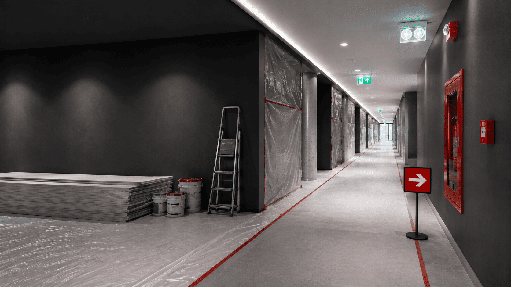 Building corridor under renovation with clear evacuation route, emergency lighting, and fire safety equipment