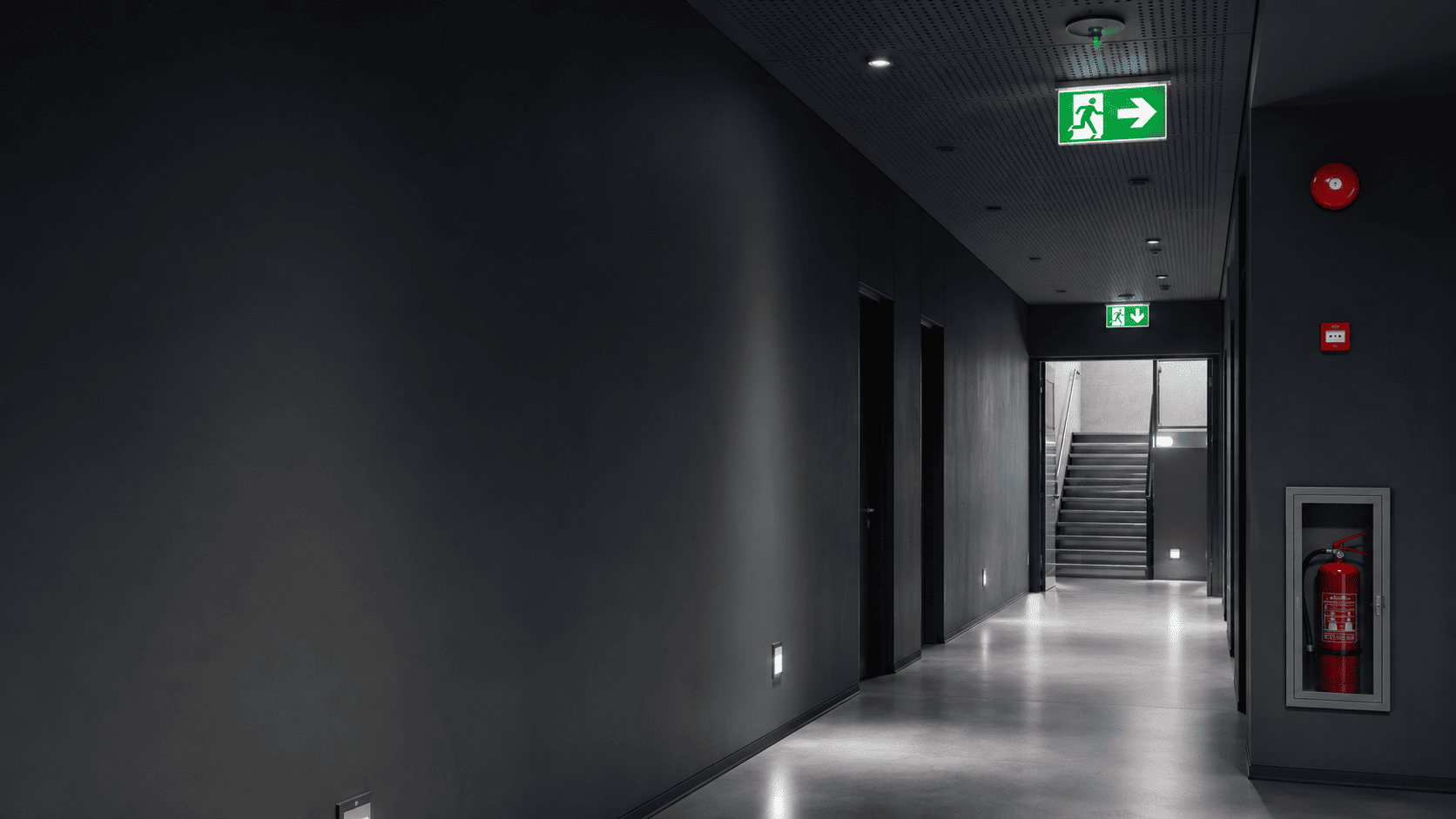 Modern corridor illuminated by emergency lighting and exit signs for evacuation route guidance