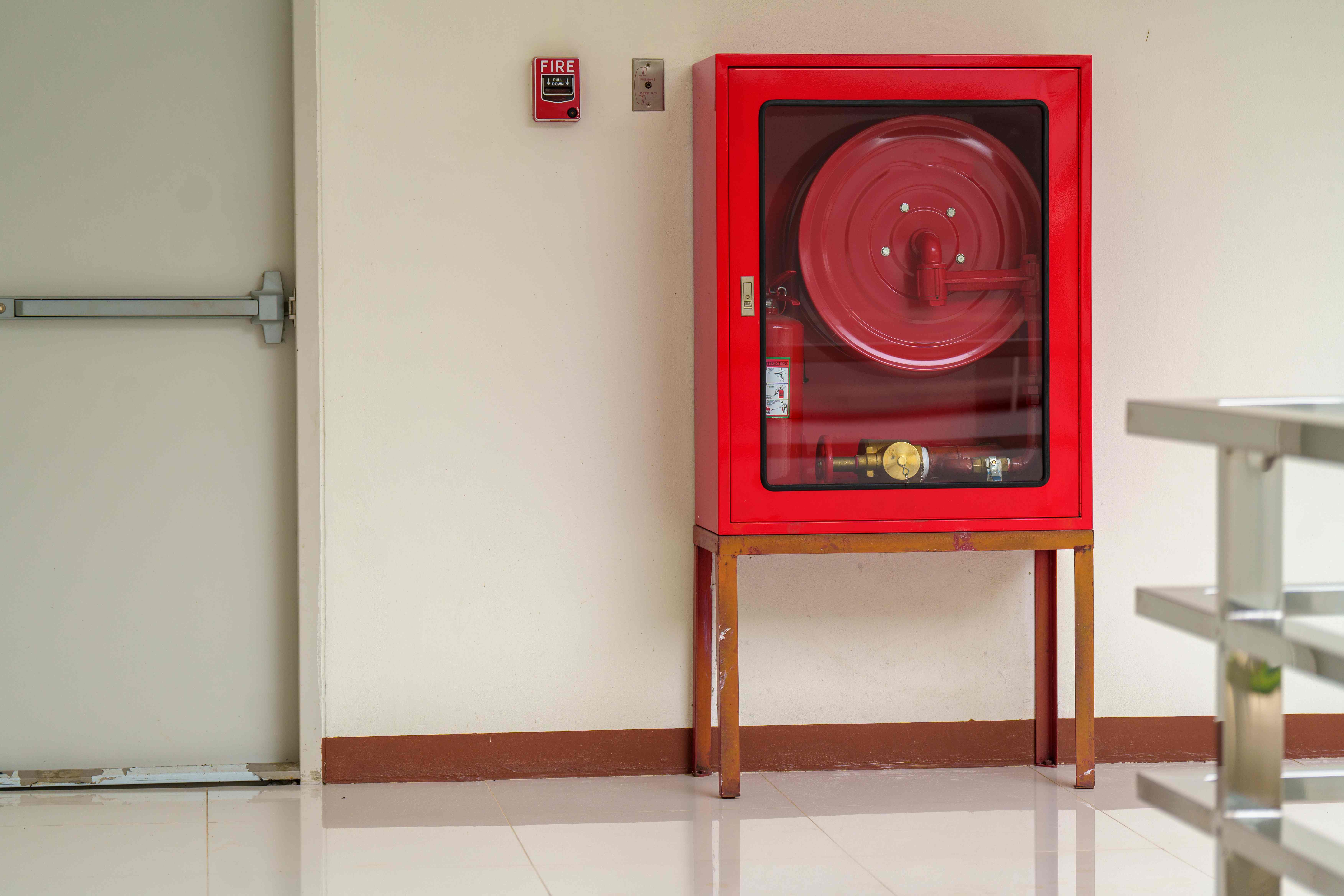 Safety technician inspecting a fire hose cabinet inside a modern building corridor